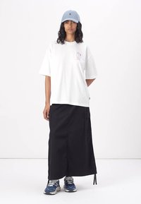 Vit bomulls t-shirt med korta ärmar och en ljusrosa grafik, tillsammans med en svart långkjol med sidofickor, och blå sneakers.