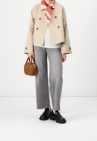 Chaqueta corta beige con botones grandes, camiseta blanca, vaqueros gris de pierna ancha y zapatos de plataforma negros. Sosteniendo un pequeño bolso marrón tejido.
