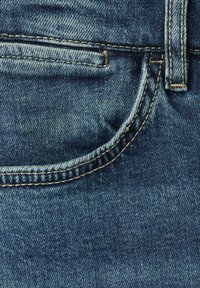 Primer plano de vaqueros de mezclilla azul oscuro, con un bolsillo curvado, costuras amarillas contrastantes y una textura suave con un ligero desgaste.