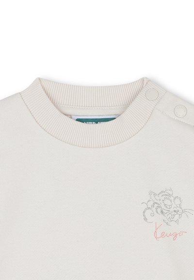 Sweatshirt en coton beige avec col rond côtelé et boutons-pression sur les épaules. Présente un design brodé gris et rose sur la poitrine.