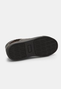 Semelle en caoutchouc noir avec un motif de grip texturé, présentant un design léger et des bords renforcés. Accent textile tissé près de la tige.