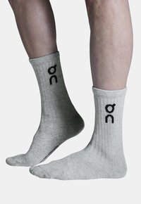 Pilkos, minkštos, raštuotos medvilninės kojinės su juodu logotipo ženklu kiekvienoje pusėje ir lygiu kojų siūlu.