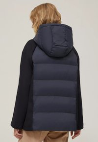 Cappotto imbottito navy con cappuccio, caratterizzato da un retro elegante e isolato e maniche nere. Texture morbida con sezioni trapuntate lungo la schiena.