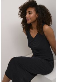 Sleeveless dark gray dress with a V-neckline, featuring gathered detailing at the waist and a ribbed texture. Smooth fabric, mid-length cut.