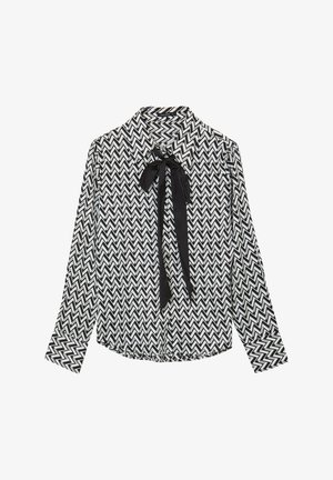 Blusa a maniche lunghe in bianco e nero con motivo zigzag a chevron, dotata di colletto e dettaglio con fiocco nero al collo.