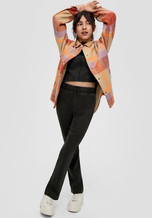 Multikolorige geruite jas in oranje, roze en beige over een zwart cropped top. Zwarte textured broek gecombineerd met witte sneakers.