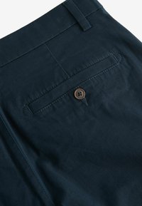 Pantalones de algodón azul marino con un bolsillo trasero que presenta un botón marrón. La tela tiene una textura suave e incluye un detalle de costura.