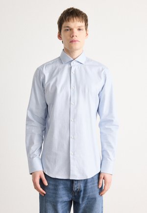 Chemise bleu clair à manches longues avec des rayures verticales, un col pointu. Le tissu semble lisse et léger.
