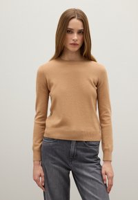 Maglione a collo rotondo di colore cammello, realizzato in maglia, con maniche lunghe e orlo a coste. Abbinato a jeans grigi a vita alta. Tessuto morbido.