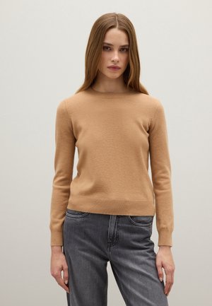 Maglione a collo rotondo di colore cammello, realizzato in maglia, con maniche lunghe e orlo a coste. Abbinato a jeans grigi a vita alta. Tessuto morbido.