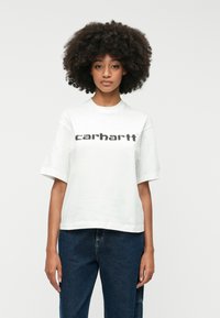 Fehér pamutpóló kerek nyakkivágással, rövid ujjal és fekete "carhartt" logóval a mellkason, sötétkék farmerrel párosítva.