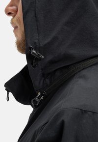 Čierna bunda s kapucňou, zipsom a nastaviteľnou šnúrkou. Materiál má hladkú textúru s matným povrchom.