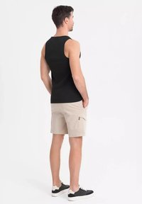 Svart ärmlös topp, ljusbeige cargoshorts med en sidoficka, och svarta sneakers med vita sulor sedda bakifrån.