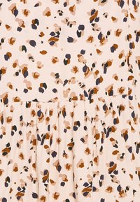 Tissu rose clair avec de petites taches irrégulières en marron, vert foncé et beige, froncé au niveau de la couture pour un effet volanté.