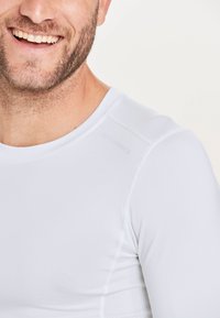 Witte lange mouwen sportshirt gemaakt van gladde, ademende stof met een ronde halslijn en ventilatie-details langs de naden.