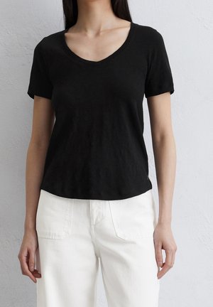 Černé tričko s krátkým rukávem a výstřihem do V, vyrobené z měkké látky. V kombinaci s bílými kalhotami s vysokým pasem, které mají zadní kapsy a volný střih.