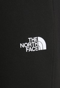 Černá tkanina s žebrovanou texturou, na které je bílá značka s nápisem "THE NORTH FACE" vedle poloviny kruhového designu.