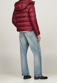 Bordowa kurtka puchowa z kapturem, z pikowanym wzorem. Do tego jasnoniebieskie jeansy o prostych nogawkach i czarne buty.