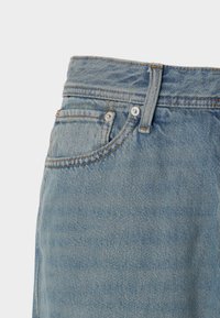 Lyseblå denimjeans med høj talje, synlige syninger og sølvhardware på forlommerne og lynlåsen.