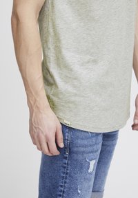 Lichtgroen T-shirt met een ronde halslijn en korte mouwen. Gecombineerd met blauwe distressed jeans. Label zichtbaar aan de zoom.