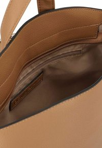 Intérieur d'un sac à main en cuir tan avec une texture lisse, comportant une poche zippée et une étiquette. Design ouvert avec un espace généreux pour les objets.