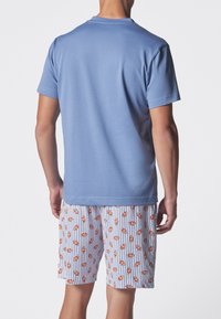 T-shirt azzurro chiaro a maniche corte con scollatura rotonda, abbinato a pantaloni corti bianchi con un motivo di pesci pagliaccio arancioni su sfondo a righe blu.
