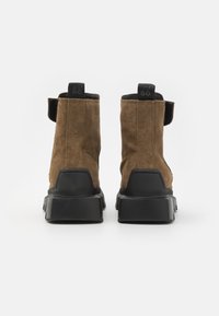 Brown suede ankle boots with black rubber soles, featuring rear pull tabs and a textured midsole for added grip.