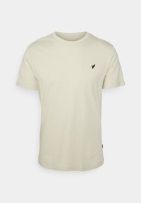 T-shirt in cotone beige chiaro con colletto rotondo, maniche corte e un piccolo logo di un uccello nero sul lato sinistro del petto. Tessuto morbido e vestibilità casual.