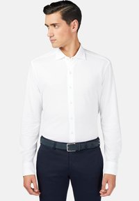 Valge pikkade varrukatega särk, millel on nööbiga krae, koos tumesiniste pükste ja sobiva vööga, millel on hõbedane kinnituse detail.