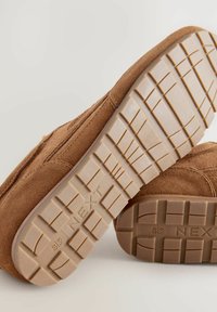Braune Wildlederschuhe mit einer strukturierten Oberfläche und Gummisohlen. Die Sohlen verfügen über ein Rautenmuster und die "NEXT"-Markierung, die für Rutschfestigkeit sorgt.