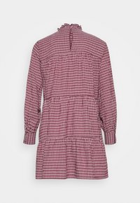 Robe à carreaux rouges et blancs avec des manches longues, un col froncé et une jupe à volants. Tissu en coton à la texture douce et fermeture à boutons dans le dos.