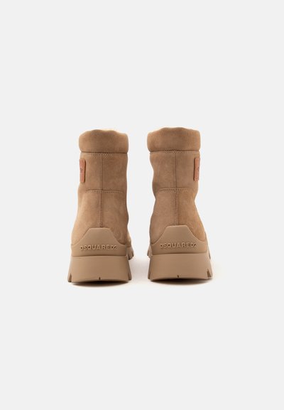 Paire de bottines en daim beige avec semelles épaisses en caoutchouc, vue de dos, avec le logo DSQUARED2 sur la languette du talon.