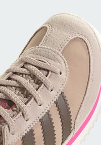 Ten bež sportska cipela s gornjim dijelom od brušene kože i tekstila, sivim prugama, teksturiranim vezicama i ružičastim detaljem na srednjem potplatu.