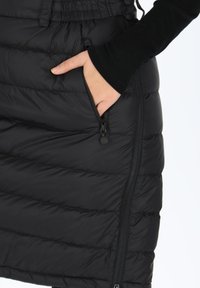 Svart puffkjol med diagonalt quiltat mönster, horisontella sömmar, dragkedjeförsedd sidficka och justerbar midja med knappar.