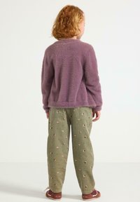 Maglione viola fuzzy con maniche lunghe, abbinato a pantaloni in corduroy verde con motivi floreali. Scarpe in pelle marrone con lacci bianchi.
