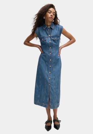 Vestido camisero de denims, hasta la rodilla, con mangas cortas y cuello tipo camisa. Presenta un cierre frontal con botones, dos bolsillos en el pecho y costuras decorativas.