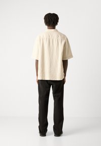 Korte mouwen, crèmekleurig shirt met een ontspannen pasvorm, gestructureerde stof en een kraag aan de achterkant. Gecombineerd met zwarte, rechte broek.