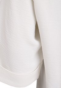 Leichtes, strukturiertes weißes Gewebe mit dezenten Falten. Verfügt über einen umgeschlagenen Saum und glatte Nähte. Keine sichtbaren Muster oder Hardware-Details.