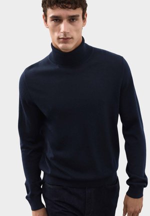 Pull en col roulé bleu marine en tissu léger, avec des manches longues, un col ajusté et une texture lisse, associé à un jean foncé.