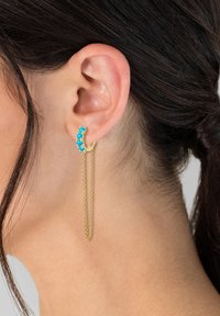 Boucle d'oreille en or avec des perles en turquoise, présentant une chute en chaîne linéaire. Texture lisse, forme circulaire et accents bleu vif.