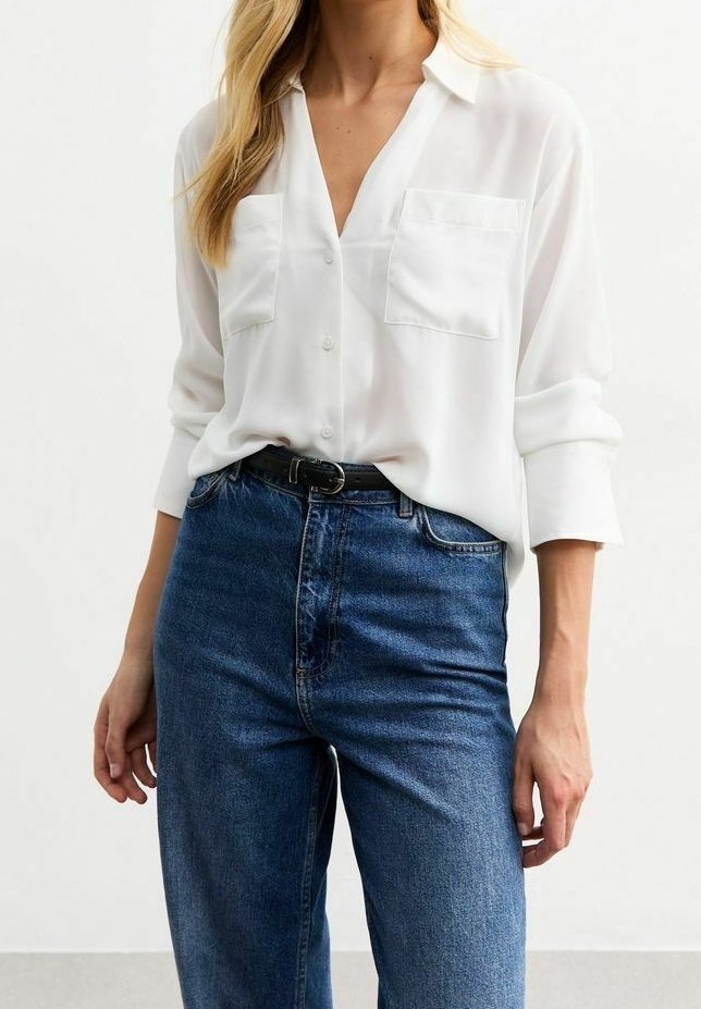 Camicia bianca a maniche lunghe con bottoni e due tasche sul petto, abbinata a jeans in denim blu a vita alta. Tessuto morbido, vestibilità rilassata.