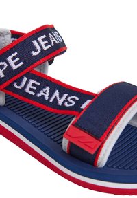 Tamsiai mėlynos sandalai su raudonais ir baltais akcentais, turintys reguliuojamas audinio juostas, pažymėtas "JEANS", ir tekstūruotą gumos padas.