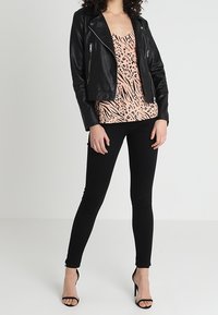 Veste de motard en cuir noir portée sur un haut rose à imprimé animal, associée à un jean skinny noir et des talons noirs à lanières.