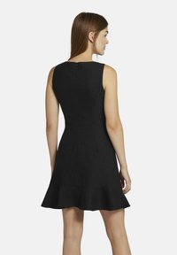 Schwarzes ärmelloses Kleid mit schwingendem Saum, das dezente Nadelstreifen und einen Reißverschluss auf der Rückseite aufweist. Der strukturierte Stoff sorgt für eine formende Passform.