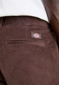 Hnedé kordové nohavice s malou nášivkou Dickies. Medzi vlastnosti patrí štandardný strih a textúrovaná rebrová tkanina, s detailom na zadnej vrecku.