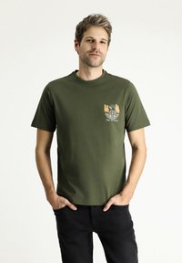 Camiseta de algodón verde oliva con cuello redondo, mangas cortas y un gráfico frontal que presenta una furgoneta, árboles y el texto "ES HORA DE VIAJAR."