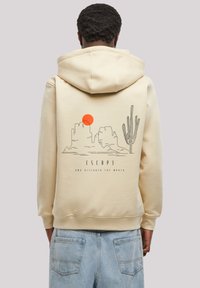 Beige hoodie featuring a graphic design of mountains, a sun, and a cactus on the back. Text reads "ESCAPE AND DISCOVER THE WORLD."