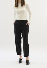 Biały prążkowany top z długim rękawem, zestawiony z czarnymi, eleganckimi spodniami i czarnymi szpilkami z zaostrzonym noskiem. Charakteryzuje się teksturowaną tkaniną i karbowanym dekoltem.