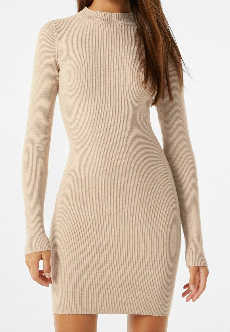 Abito a maglia a coste, maniche lunghe, di colore beige chiaro. Design aderente con colletto alto, texture morbida e maniche lunghe. Silhouette fino al ginocchio.
