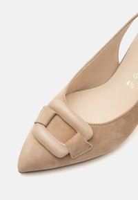 Ballerine beige en daim à bout pointu avec une grande boucle carrée assortie sur le dessus et un design slingback ouvert à l’arrière.